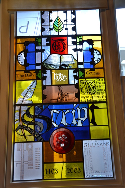 Stained glass window, a colourful abstract design with panels featuring different typefaces, the Stationers' Company crest, and Caxton's initials.