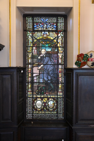 Stained glass window featuring the classic portrait of Shakespeare. The window is surrounded by the oak panelling and armorial shields of Shakespeare's Hall.